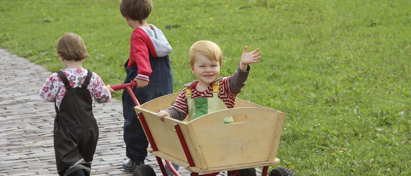 Kind in bolderkar die voort wordt getrokken door twee andere kinderen