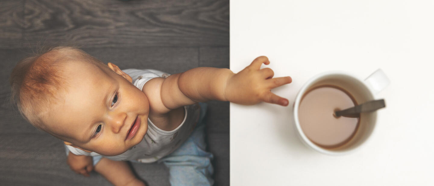 Baby reikt naar kop thee op tafel