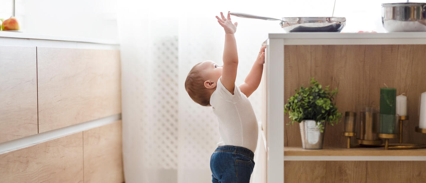 Baby reikt naar koekenpan op het fornuis