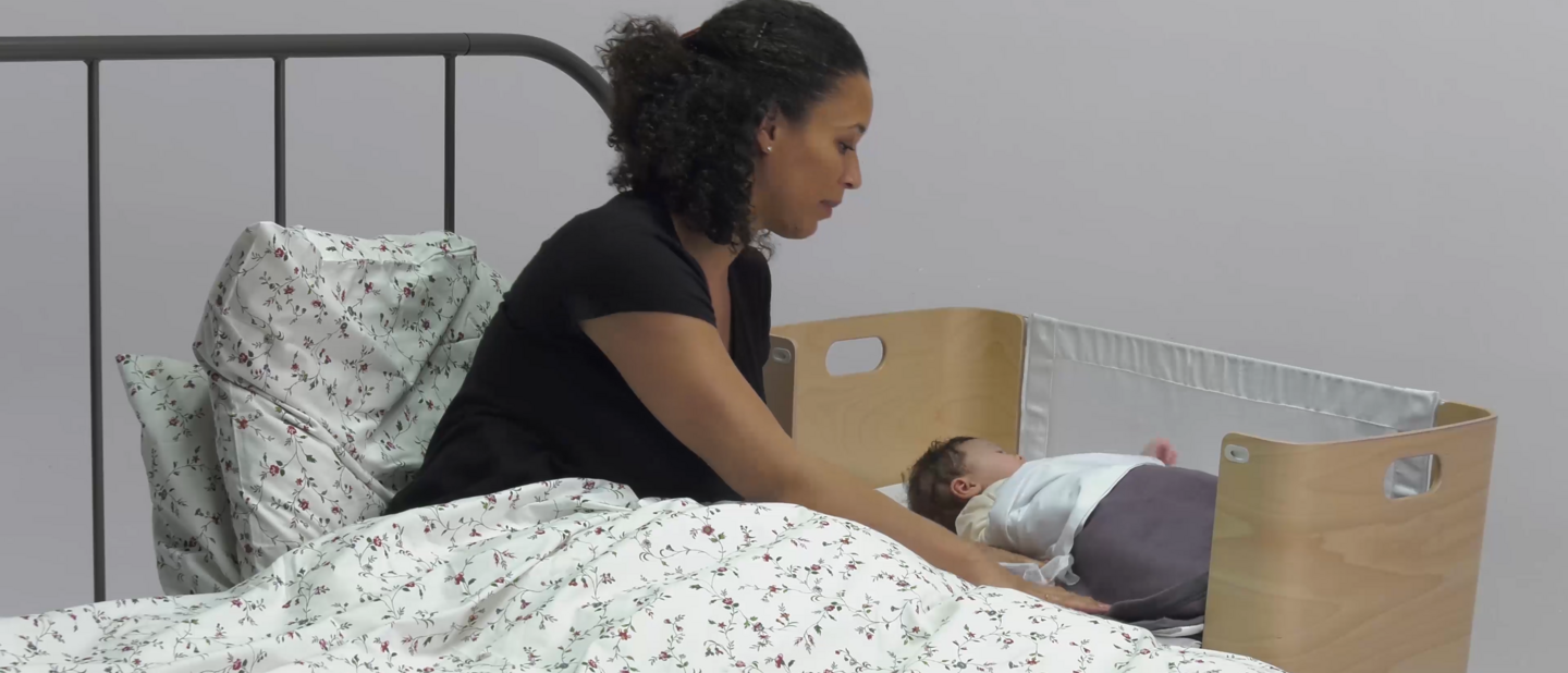 Moeder in bed met baby in co-sleeper