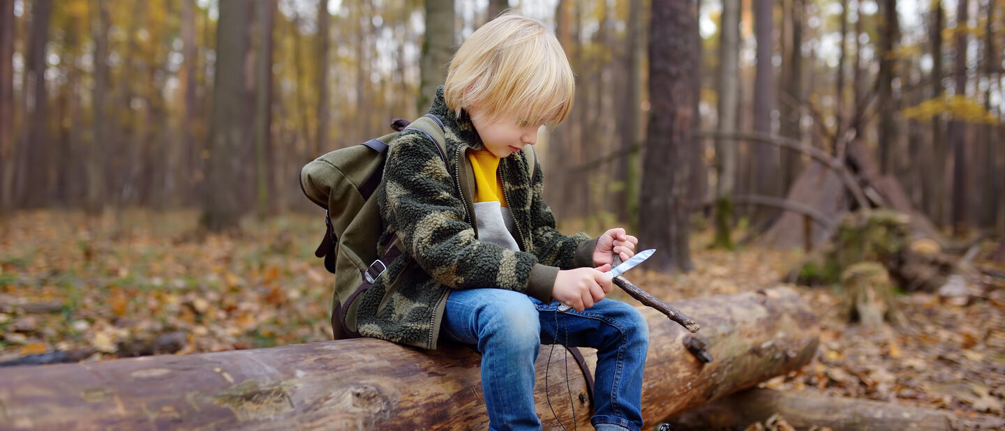 Scout zit in bos en slijpt tak